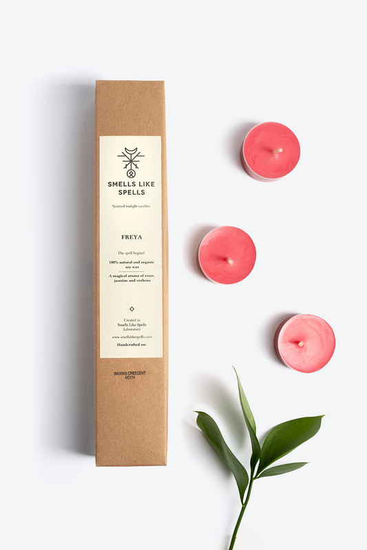 Scented tealight candles FREYA with natural aromas of verbena, jasmine, and rose in eco-friendly packaging next to green leaves.