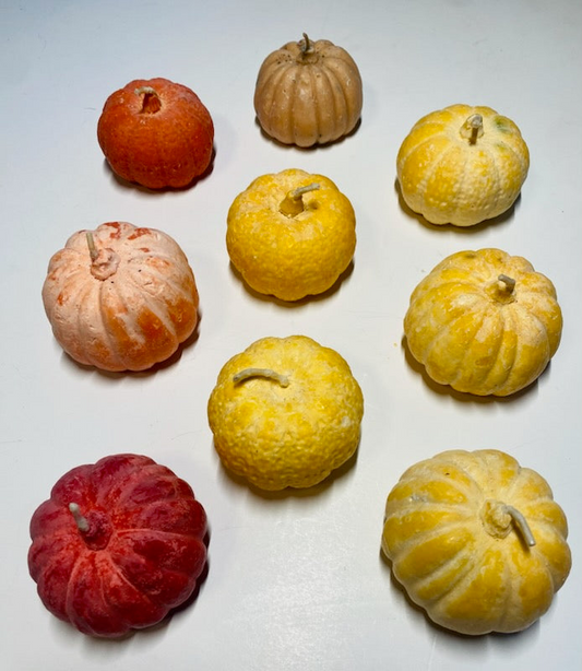 Assorted warm-colored pumpkin soy candles shaped like small pumpkins with textured surfaces and candle wicks.