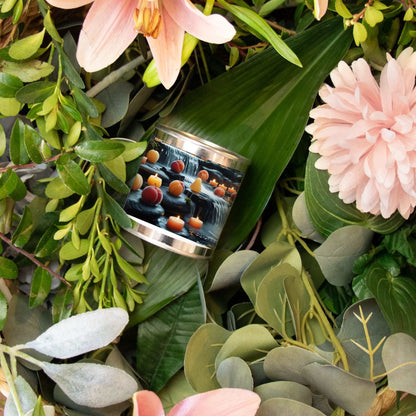 Hand-poured 8 oz Candle Paint Can with artistic label nestled among green leaves and soft pink flowers